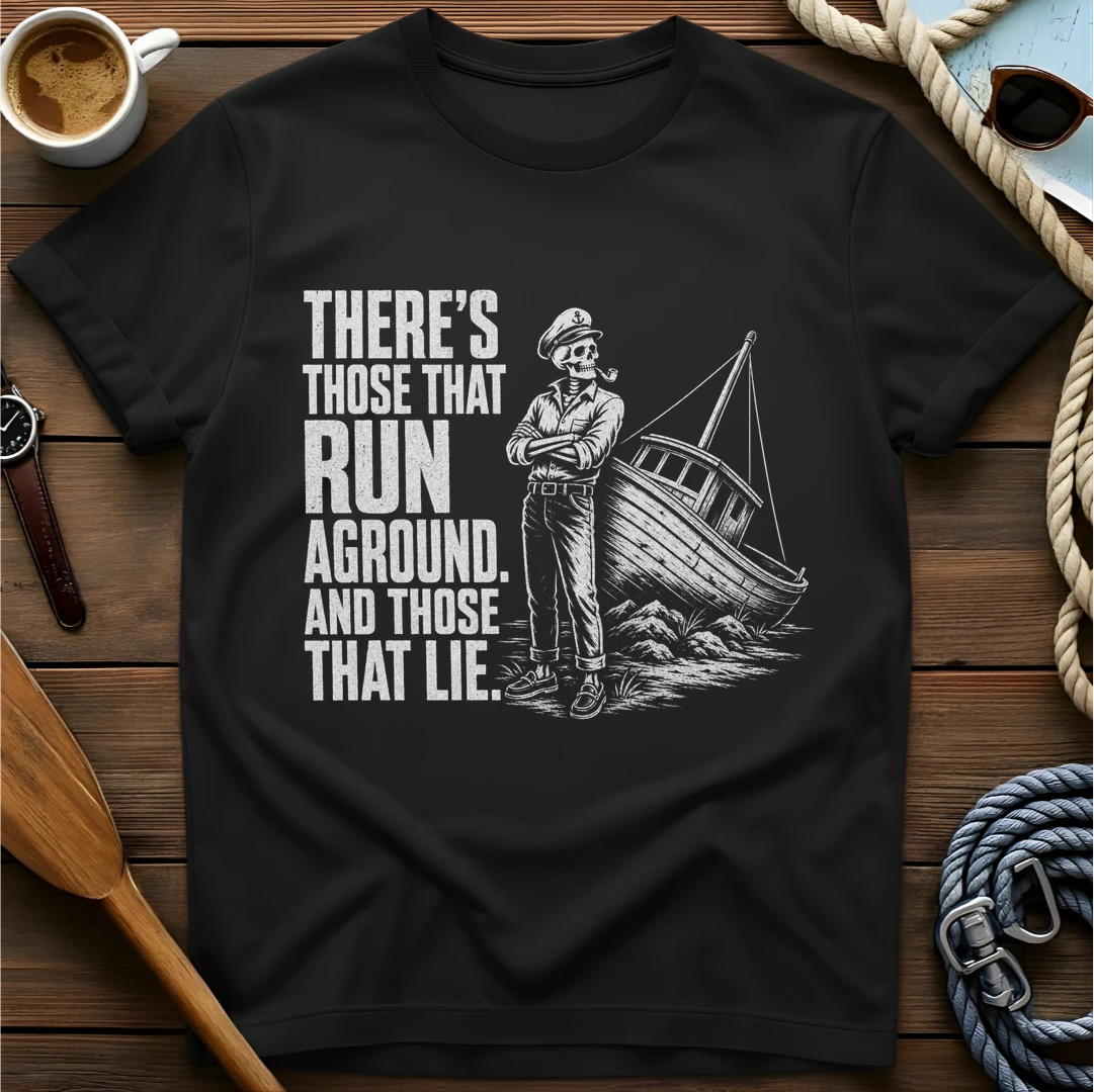 T-shirt with a skeleton captain smoking a pipe beside a sailboat run aground on rocks and text reading 'There's those that run aground. And those that lie.'