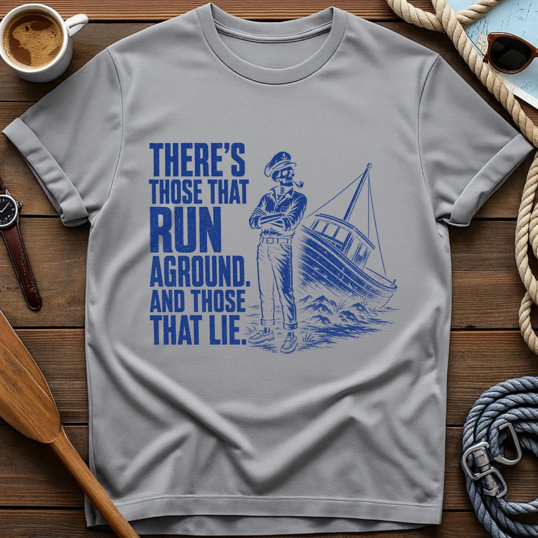 T-shirt with a skeleton captain smoking a pipe beside a sailboat run aground on rocks and text reading 'There's those that run aground. And those that lie.'