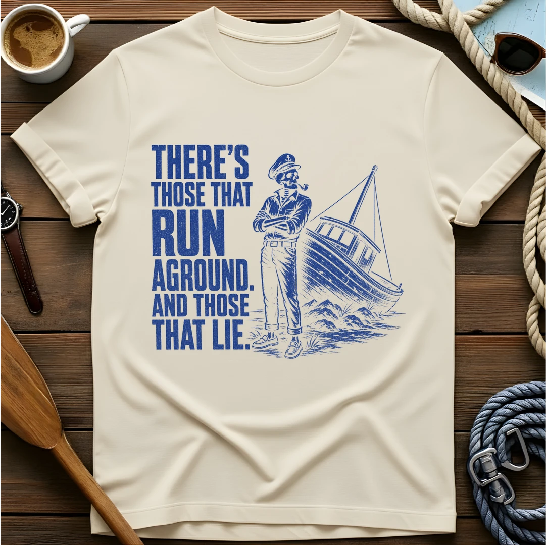 T-shirt with a skeleton captain smoking a pipe beside a sailboat run aground on rocks and text reading 'There's those that run aground. And those that lie.'
