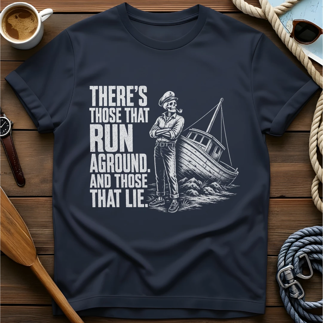 T-shirt with a skeleton captain smoking a pipe beside a sailboat run aground on rocks and text reading 'There's those that run aground. And those that lie.'